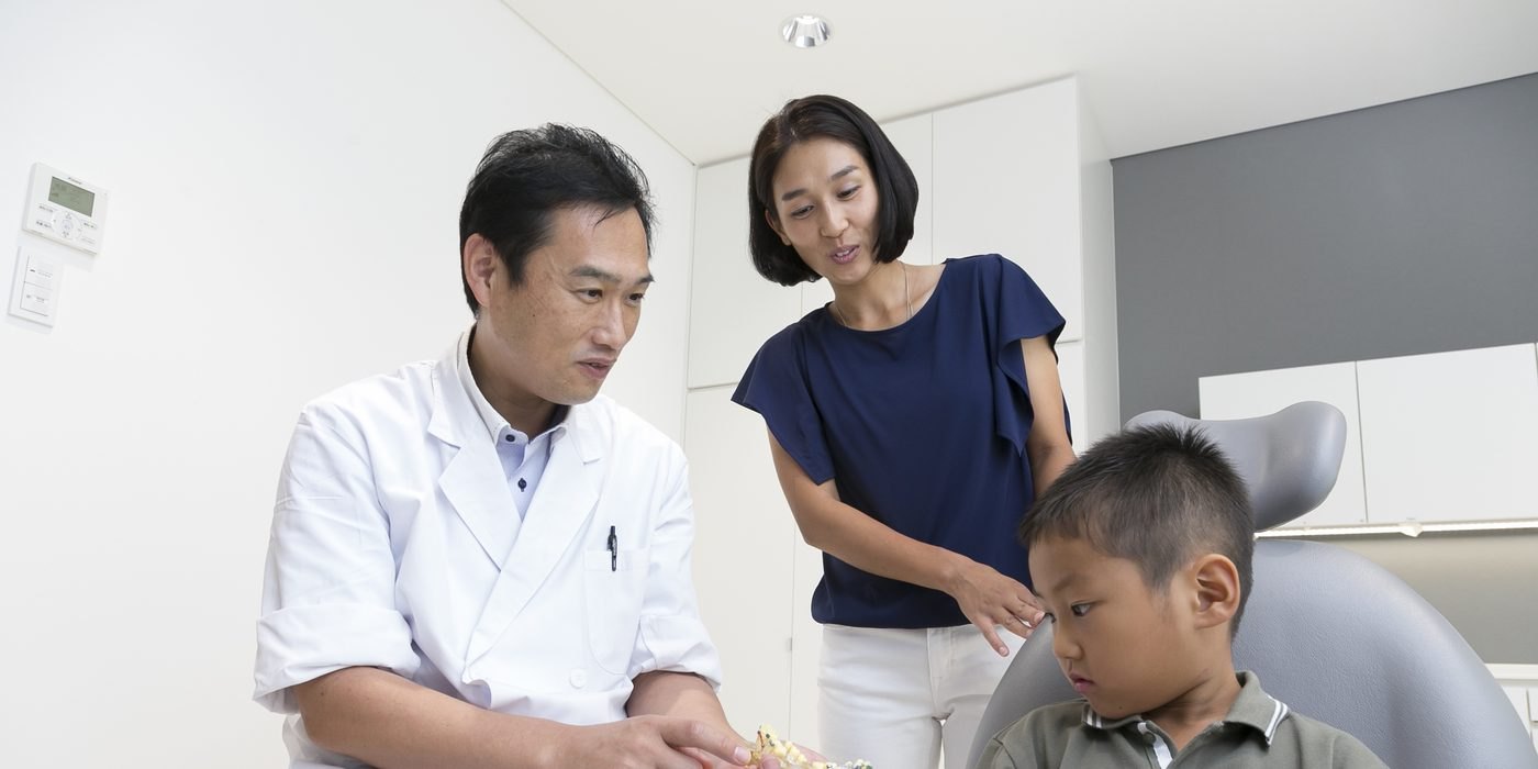 歯の模型を見せながら、お母さんとお子さんに説明する矯正専門医 菅崎弘幸