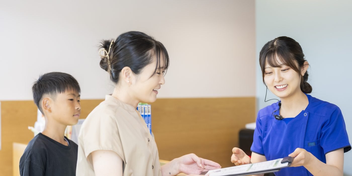 受付で、お母さんと男の子に笑顔で書類を渡すスタッフ